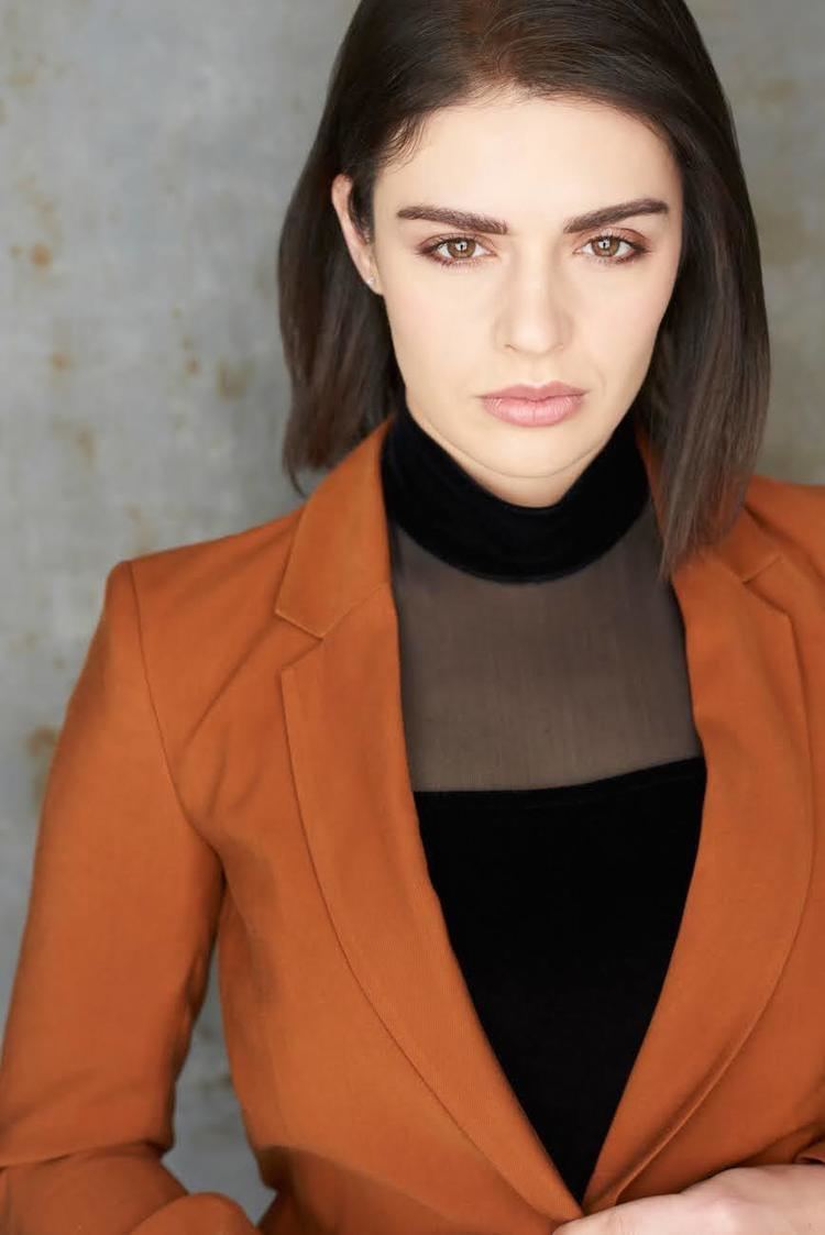 Tatiana Zappardino looking serious in her short hair while wearing an orange blazer and black inner blouse
