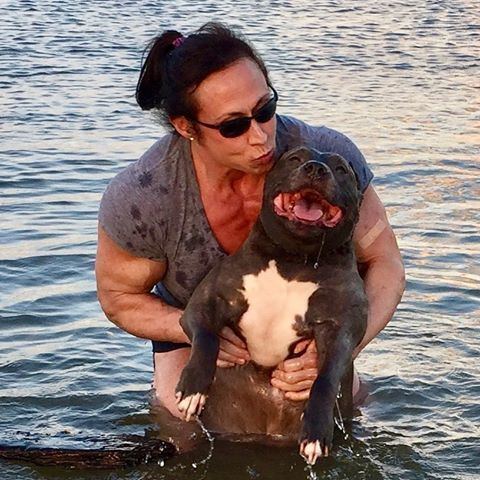 Tazzie Colomb carrying her dog while at the beach and wearing a gray t-shirt and black sunglasses