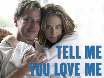 Poster of Tell Me You Love Me, a 2007 American cable television drama series starring Tim DeKay smiling and Ally Walker is with a serious face while jugging Tim. Tim is wearing a white shirt while Ally is wearing a white robe.