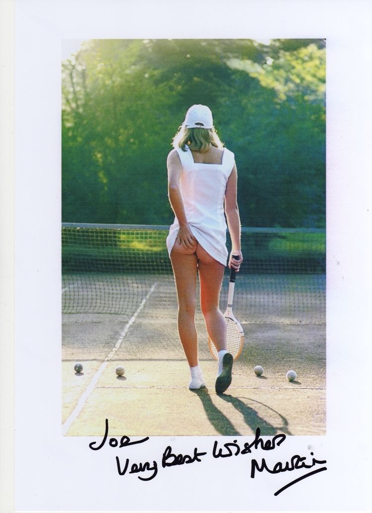 A female tennis player holding a racket, showing her butt without underwear, and wearing a white sleeveless mini dress and rubber shoes with an autograph on the bottom