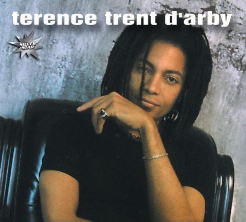 Terence Trent D'Arby with a tight-lipped smile and box braid while wearing a black t-shirt, bracelet, and ring