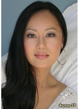 Teresa Cheung smiling closed mouth and wearing a white dress along with large earrings.