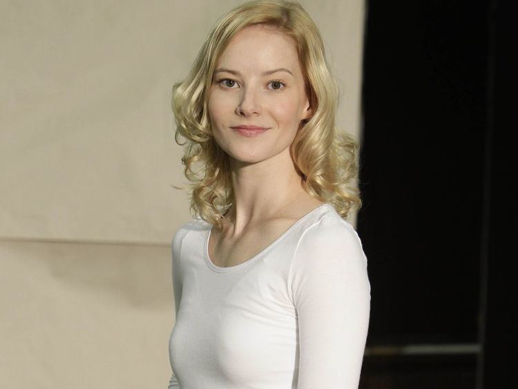 Teresa Weißbach with a tight-lipped smile and blonde curly hair while wearing a white long sleeve blouse