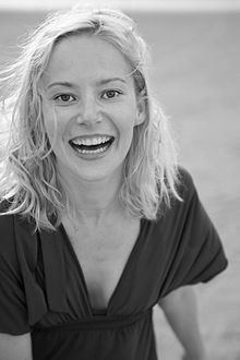 Teresa Weißbach laughing with blonde shoulder-length hair and wearing a blouse with a plunging neckline
