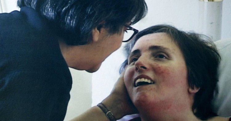 Terri Schiavo smiling while lying on the bed and looking at her mother, Mary Schindler who is wearing a black blouse and eyeglasses