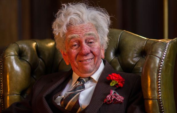 Paul Whitehouse as Unlucky Alf smiling and wearing a formal suit and tie in a scene from 1994 BBC show The Fast Show.