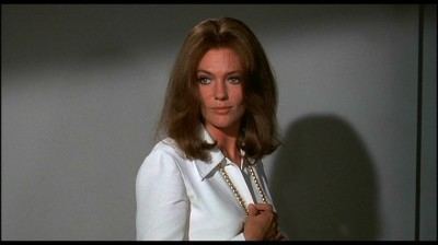 Jacqueline Bisset as Anna smiling with her blonde hair down and wearing a white long sleeve blouse and a pearl necklace