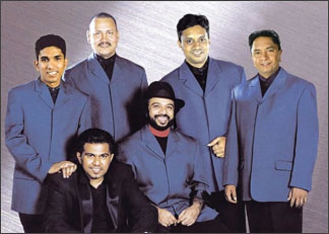 The Gypsies' members smiling all together while wearing a coat and black inner shirt