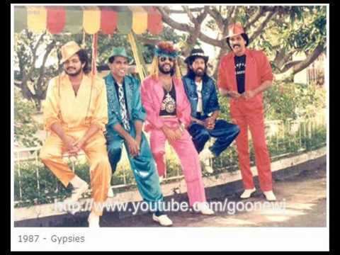 The Gypsies' members leaning on a fence while wearing hats, colorful long sleeves, and pants