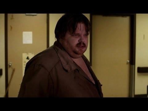 Scene from the movie "The Hospital" featuring a fat guy with a scary face and wearing a brown polo shirt.
