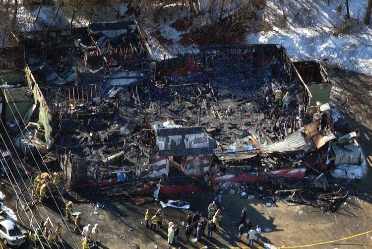 From the air, the burned-out remains of the Station nightclub where at least 60 people died in a late-night fire in West Warwick, Rhode Island. As seen, firefighters, medics, and police officers are still on the scene to clear the area.