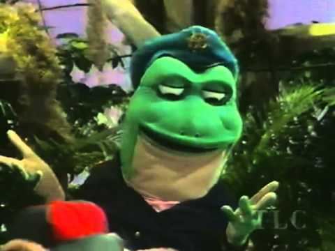 Ribbit E. Lee wearing a frog costume, with a black coat and a green hat in a scene of "The Swamp Critters of Lost Lagoon"
