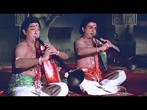 Shivaji Ganesan is topless while playing the flute and wearing white pants in a movie scene from Thillana Mohanambal (1968 film).