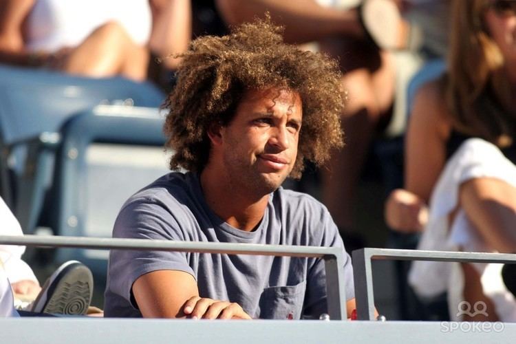 Thomas Blake looking afar while sitting on the bleachers, with kinky hair, and wearing a gray t-shirt