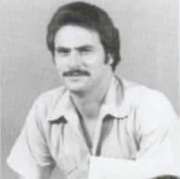 In black and white Thomas DeSimone is serious, sitting in front of white background, has black hair and a mustache wearing a white polo.