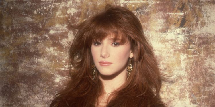 Tiffany Darwish looking serious with her wavy hair down while wearing a black coat and dangling earrings