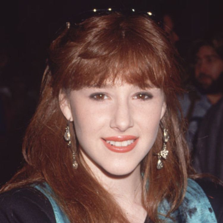 Tiffany Darwish smiling and wearing a black sleeves and blue vest with dangling earrings