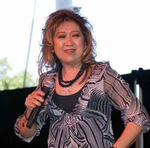 Tillie Moreno smiling while holding a microphone and wearing a black and white blouse and black necklace