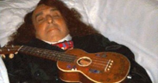 Tiny Tim lying on his coffin, wearing a suit and a ukelele on top of him.