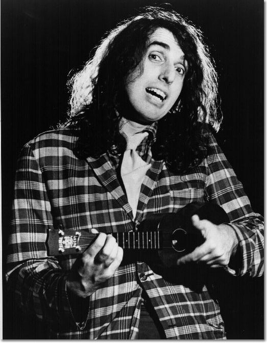 Tiny Tim with curly hair, wearing a checkered suit and playing a ukelele.