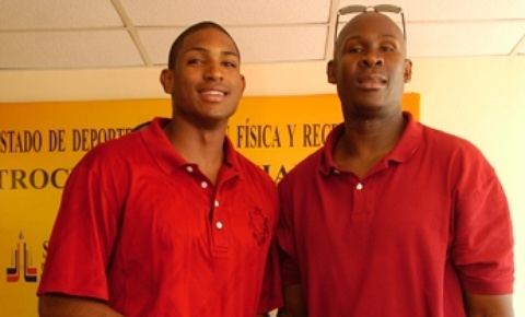 Al Horford (left) is smiling, has black hair and a mustache, wearing a red polo shirt. Tito Horford (right) is serious, bald, wearing glasses on his head and a red polo shirt.