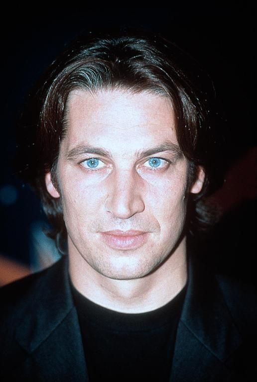 Tobias Moretti with blue eyes and wearing a black shirt underneath a black coat