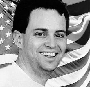 Todd Beamer smiling while behind him is the flag of the United States of America