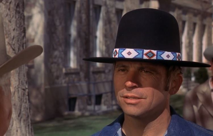 Tom Laughlin talking to someone while wearing a black hat, t-shirt, and denim jacket in a scene from the 1971 film, Billy Jack