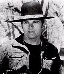 Tom Laughlin looking afar while wearing a black hat, t-shirt, and denim jacket in a scene from the 1971 film, Billy Jack