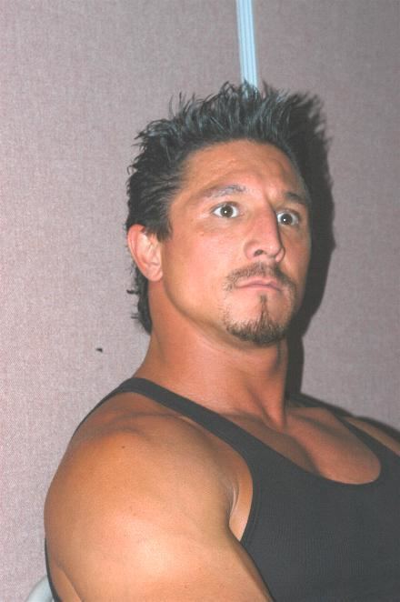 Tommy Gunn looking at something while wearing a black sleeveless shirt.