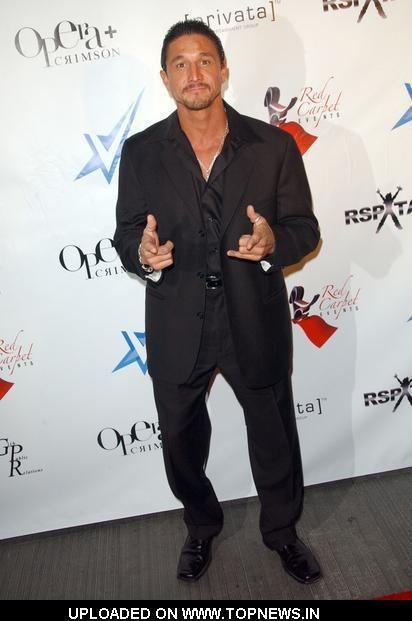 Tommy Gunn smiling and posing at an event and wearing a black formal attire.