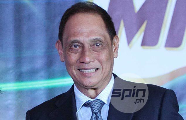 Tommy Manotoc smiling and wearing a white-striped shirt under a black coat and blue necktie