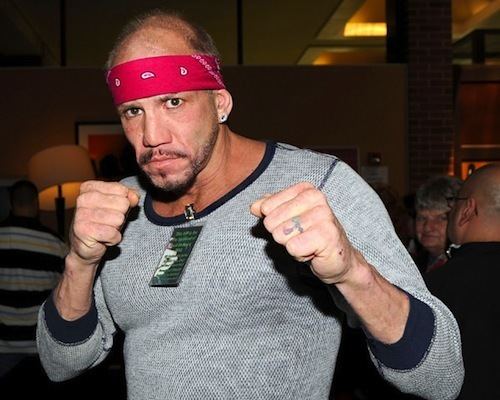 Tommy Morrison showing a boxing pose while wearing black and gray sweatshirt and red bandana