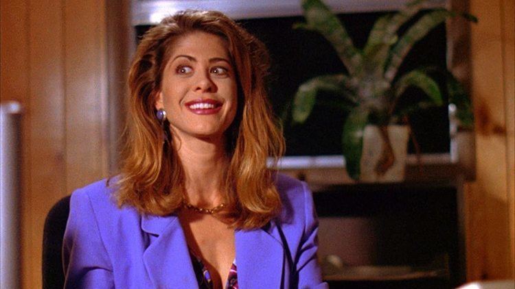 Tonie Perensky smiling while wearing a blue coat, necklace, and earrings in a scene from the 1995 film, Texas Chainsaw Massacre: The Next Generation