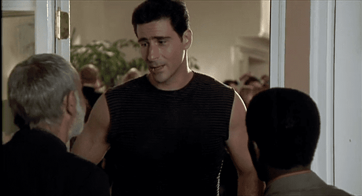 Tony Ganios is talking at the two men in a movie scene from The Wanderers, a 1979 American comedy-drama film, wearing a black sleeveless shirt.