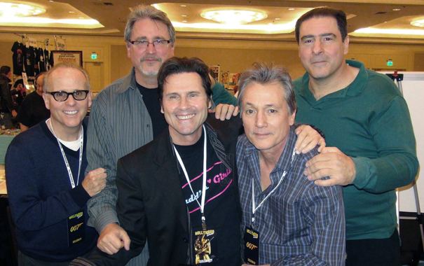 Dan Monahan, Mark Herrier, Cyril O'Reilly, Scott Colomby, and Tony Ganios (from left to right) are all smiling. Dan is wearing eyeglasses and an ID card over his blue long sleeve shirt, Mark is also wearing eyeglasses and gray stripe long sleeves over a black shirt, Cyril is wearing an ID card over his black coat and black printed shirt, Scott is wearing an ID card over his checkered long sleeves, and Tony is wearing a green collared long sleeve shirt.