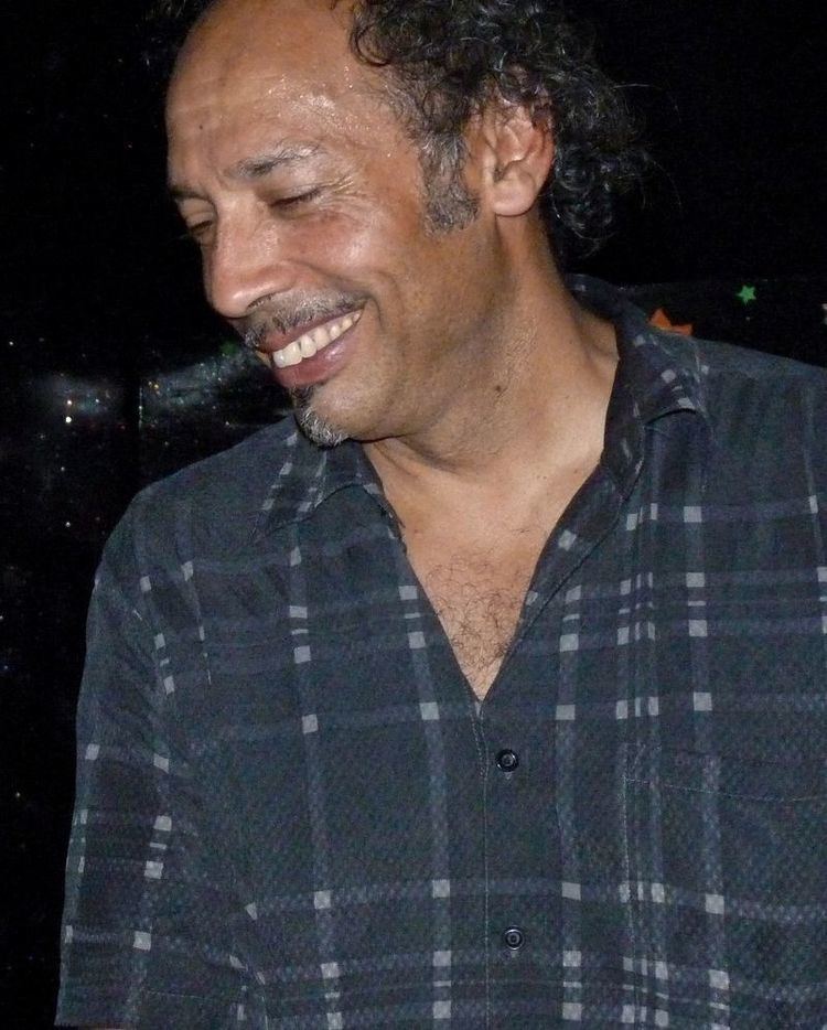 Tony Garnier smiling, with curly hair, and wearing a checkered gray long sleeves.