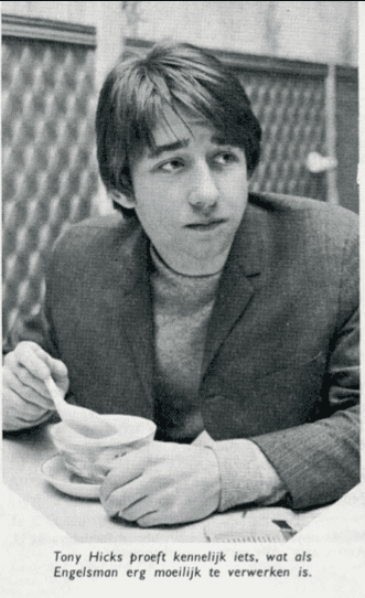 Tony Hicks holding a spoon and bowl on the table while looking at the right side, with a serious face, and he is wearing a shirt under a coat