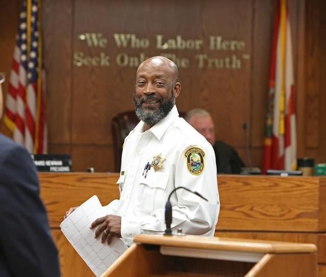 Tony Nathan smiling while holding documents inside the Miami-Dade courtroom in a bailiff uniform