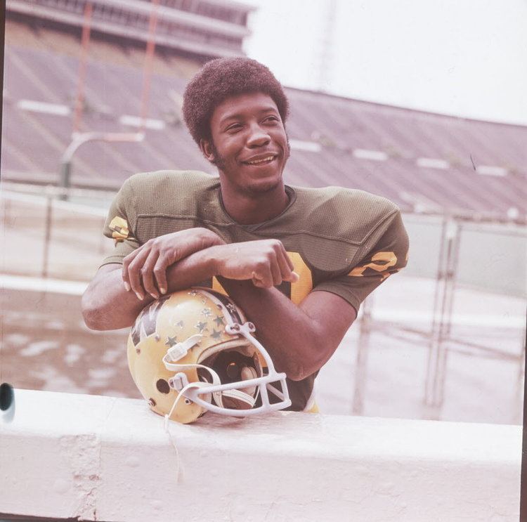 Tony Nathan smiling at the Legion Field while resting his arms on the top of his football hat and wearing his jersey