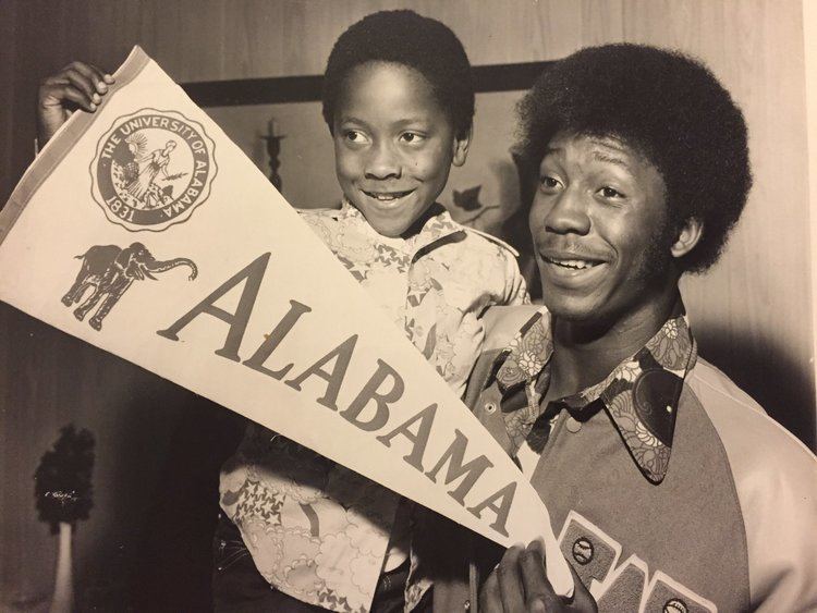 Tony Nathan smiling while carrying his youngest brother, Cedric, after he signed a scholarship to play for the University of Alabama in December 1974.
