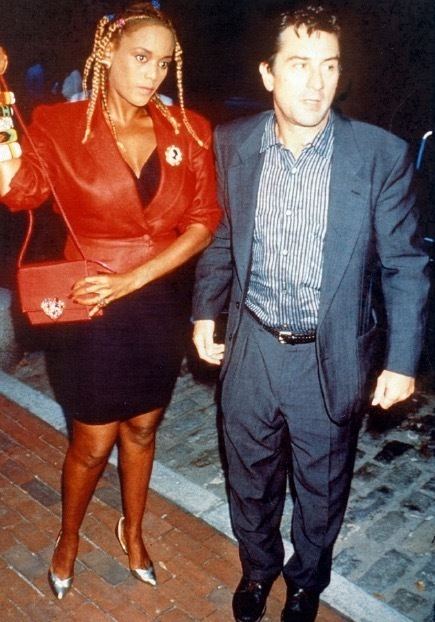 Robert De Niro wearing blue coat and striped long sleeves & Toukie Smith in her braided hair, red coat, black dress and red bag