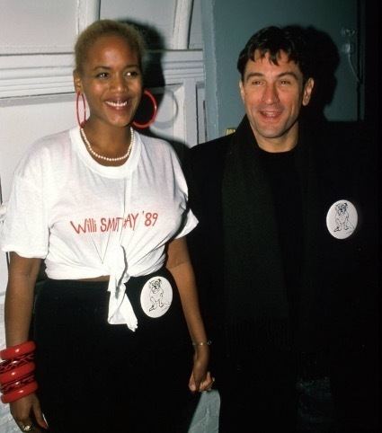 Toukie Smith smiling while wearing white shirt and black pants with Robert De Niro in his black coat and black inner shirt