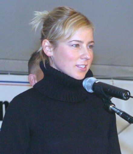 Traylor Howard speaking in front of a microphone with blonde hair and wearing a black turtle neck knitted jacket