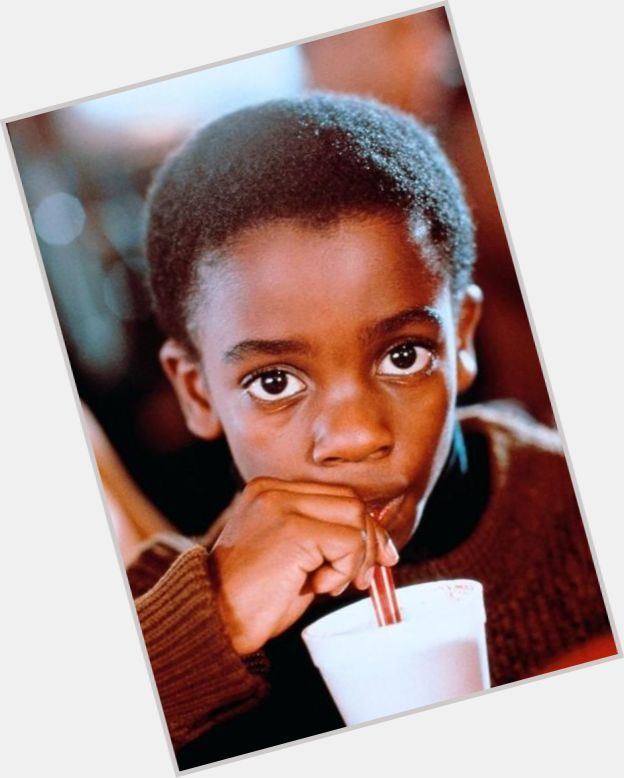 Trent Cameron at a young age, wearing a brown knitted sweatshirt while sipping a drink.