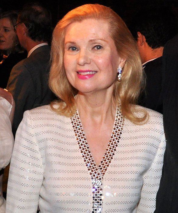 Tricia Nixon Cox smiling while wearing a white and silver long sleeve blouse and earrings