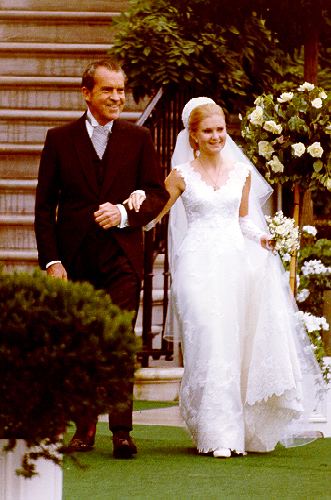 Tricia Nixon walking down the aisle with her father while she is wearing a wedding gown