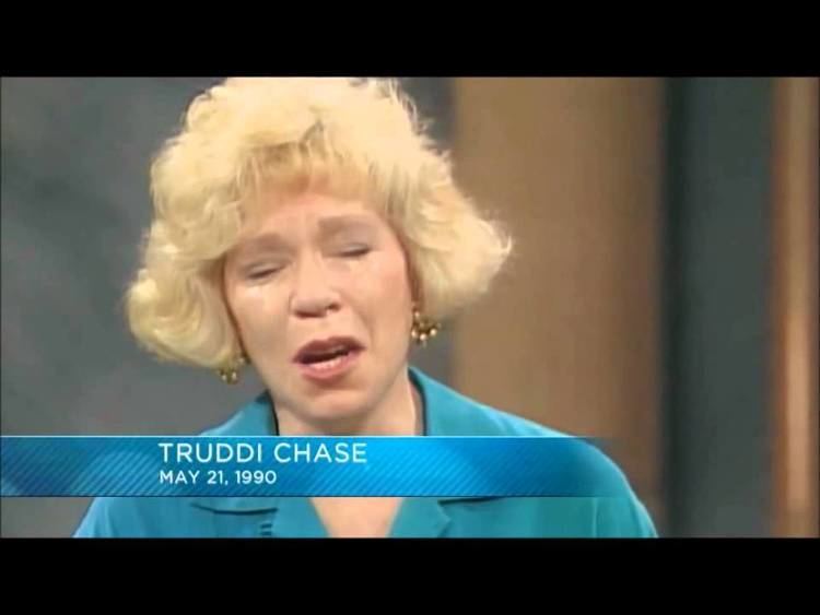 Truddi Chase crying in an interview and wearing a blue blouse and some gold earrings.