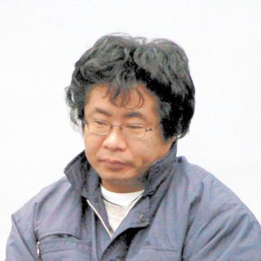 Tsutomu Miyazaki with a sad face, wearing eyeglasses, a jacket, and a white shirt.