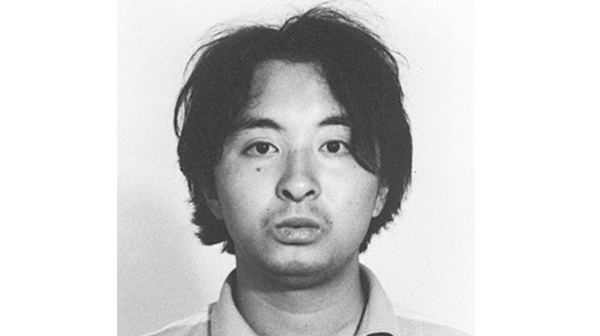 Tsutomu Miyazaki with a mole on his face, long black hair, and wearing a polo shirt.
